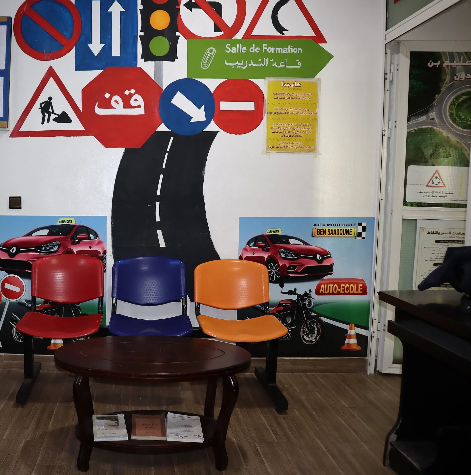 Coin d’attente coloré : sièges rouge, bleu et orange devant la fresque de panneaux « Salle de formation »